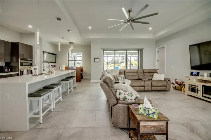 Living room featuring a raised ceiling, recessed lighting, concrete floors, and a ceiling fan