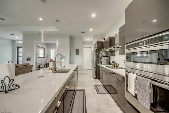 Kitchen with stainless steel appliances, pendant lighting, open floor plan, modern cabinets, and light stone counters