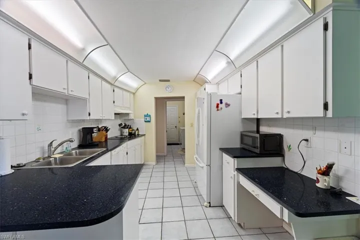 Kitchen featuring white cabinets, decorative backsplash, light tile patterned floors, and sink