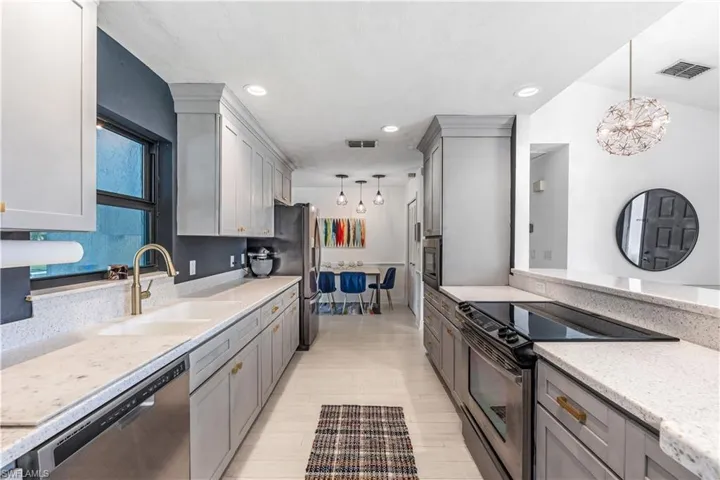 Kitchen with appliances with stainless steel finishes, gray cabinetry, sink, pendant lighting, and light hardwood / wood-style flooring