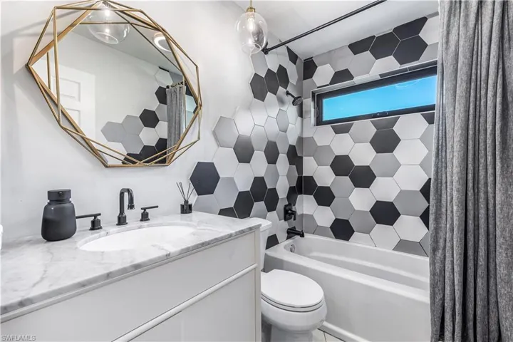 Full bathroom featuring vanity, toilet, tiled shower / bath, and tile walls