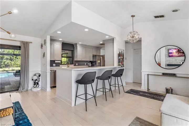 Kitchen featuring gray cabinetry, lofted ceiling, hanging light fixtures, and stainless steel fridge with ice dispenser