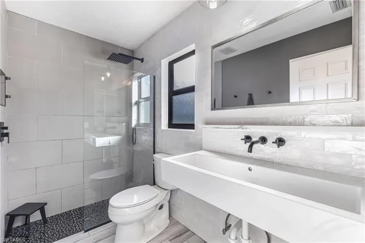 Bathroom featuring a tile shower, sink, wood-type flooring, tile walls, and toilet