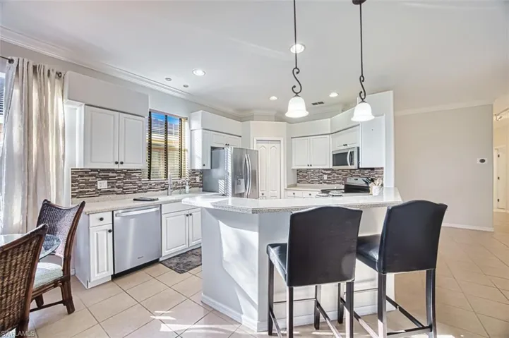 Kitchen featuring crown molding, appliances with stainless steel finishes, decorative backsplash, light tile patterned floors, and white cabinetry