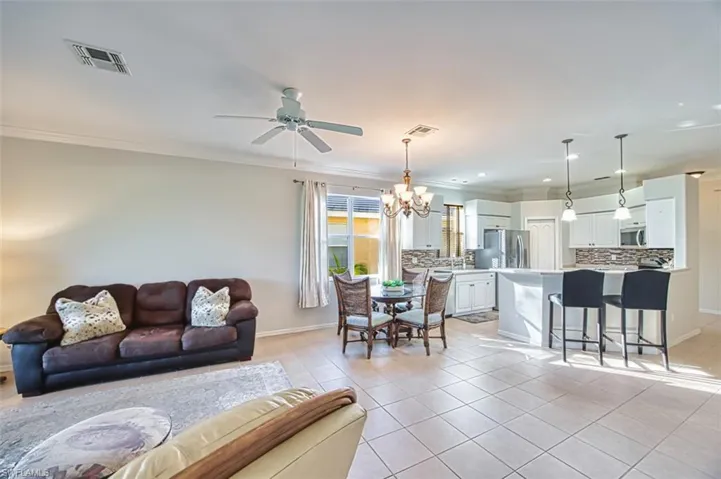 Living area with light tile patterned floors, a chandelier, crown molding, ceiling fan, and recessed lighting