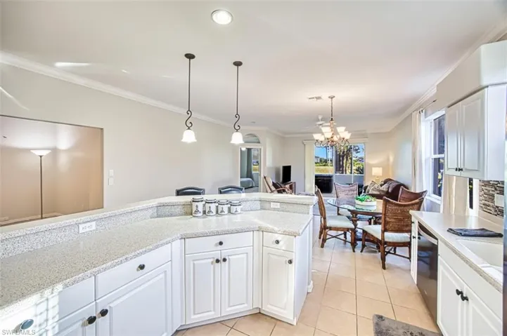Kitchen featuring white cabinetry, crown molding, hanging light fixtures, light tile patterned floors, and light stone counters