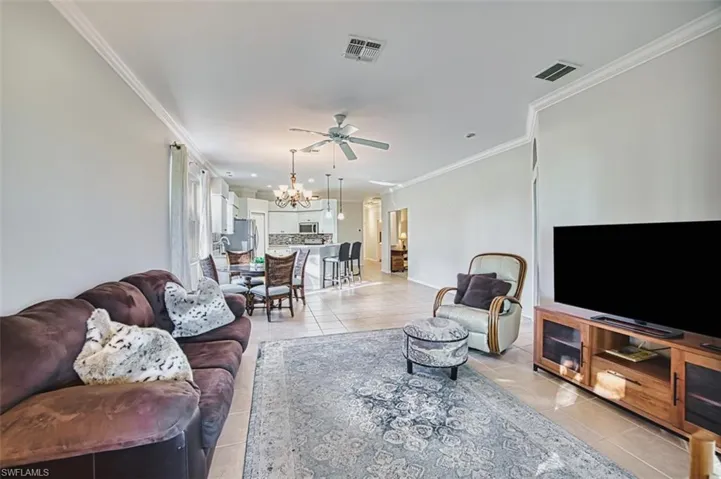 Living room featuring ornamental molding, light tile patterned floors, ceiling fan, and a chandelier