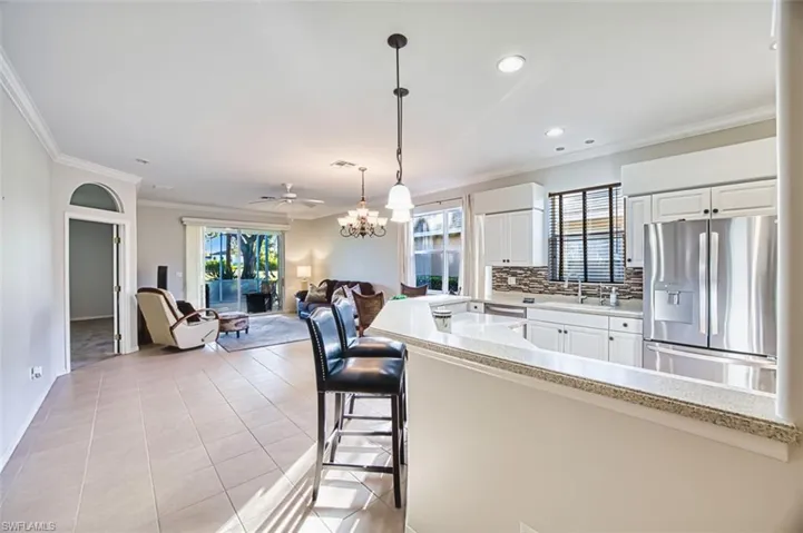 Kitchen featuring stainless steel appliances, a chandelier, decorative light fixtures, crown molding, and white cabinetry