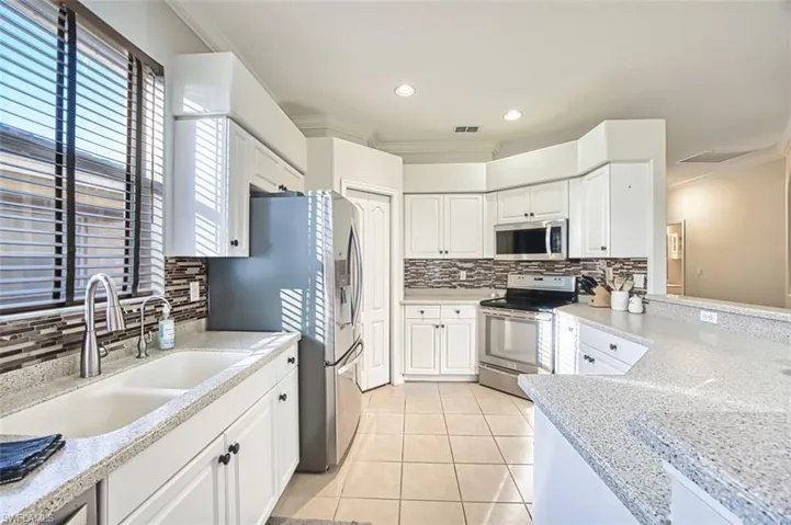 Kitchen featuring ornamental molding, decorative backsplash, white cabinetry, stainless steel appliances, and light tile patterned floors