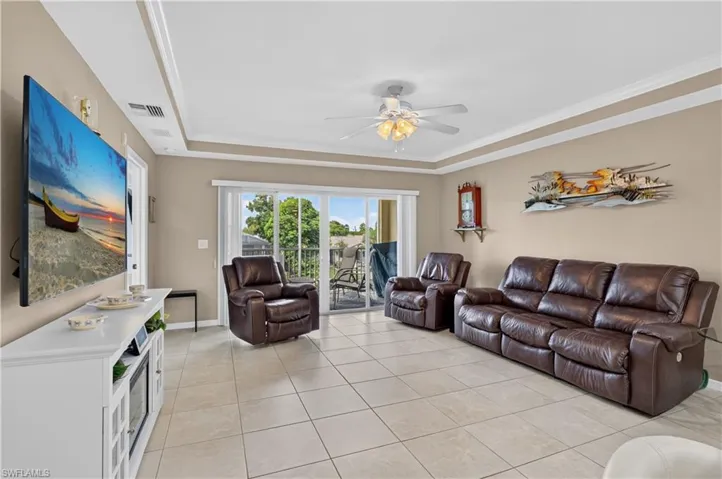 Tray ceiling with crown molding, ceiling fan with light fixture, neutral wall paint, tile flooring, and sliding glass doors