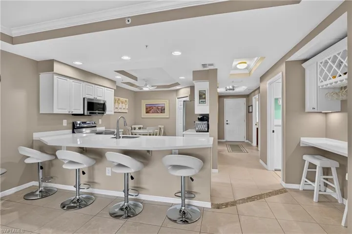 Kitchen featuring white cabinetry, stainless steel appliances, a large island with a sink, and tile flooring