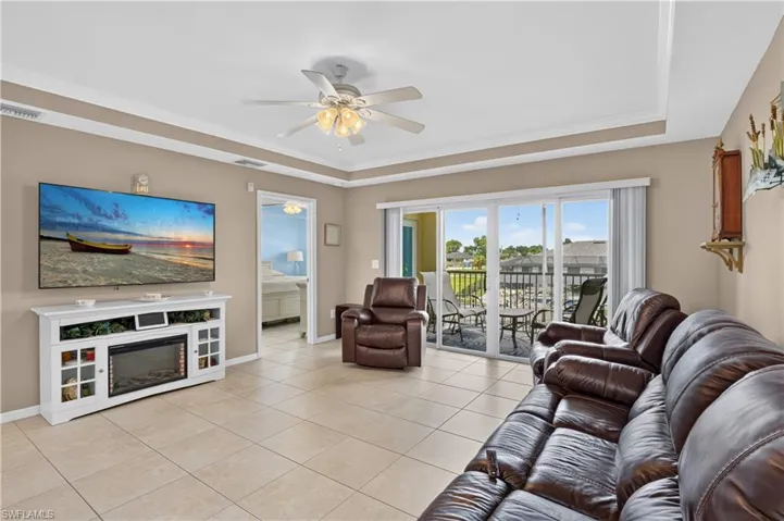 Recessed tray ceiling with crown molding, tiled flooring, ceiling fan, and sliding glass doors leading to a private balcony