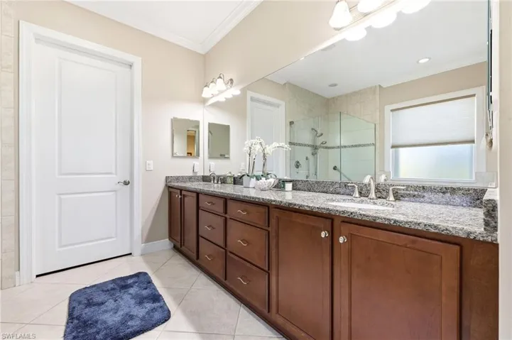 Full bathroom with double vanity, a stall shower, crown molding, and light tile patterned floors