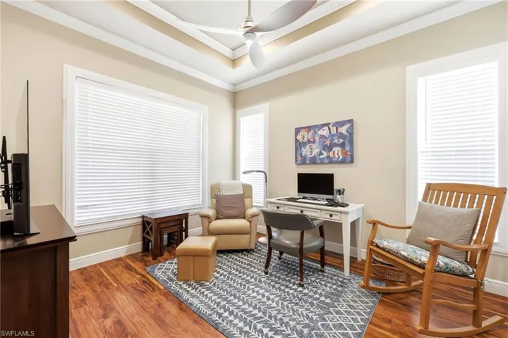 Office space with ornamental molding, ceiling fan, wood finished floors, and a tray ceiling