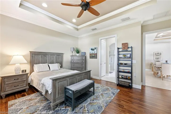 Bedroom with a tray ceiling, crown molding, dark wood-style flooring, ceiling fan, and recessed lighting