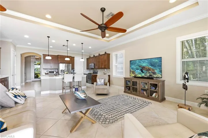 Living room featuring arched walkways, a ceiling fan, ornamental molding, plenty of natural light, and a raised ceiling