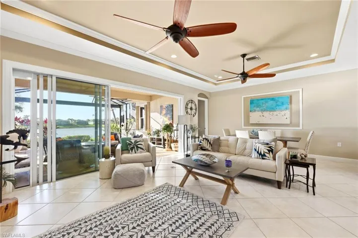 Living area with crown molding, ceiling fan, a water view, a tray ceiling, and arched walkways