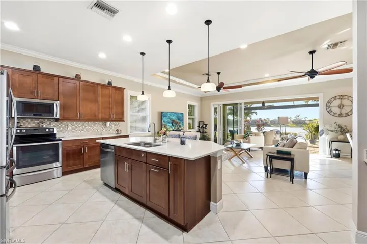 Kitchen featuring stainless steel appliances, light stone counters, decorative light fixtures, ornamental molding, and open floor plan