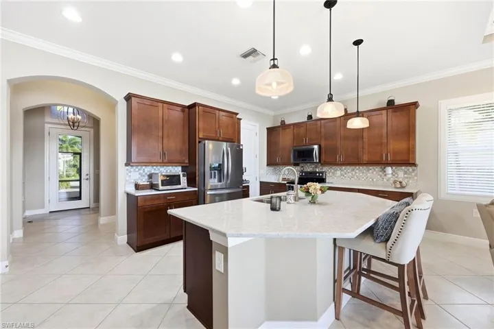 Kitchen featuring plenty of natural light, arched walkways, stainless steel appliances, light tile patterned flooring, and crown molding