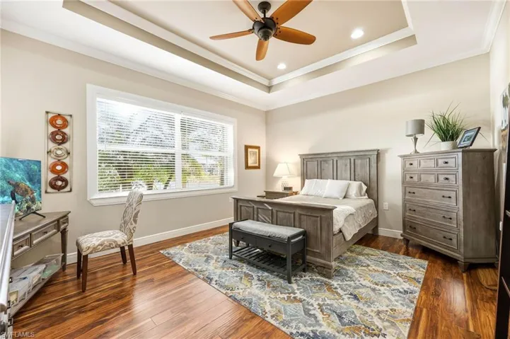 Bedroom featuring dark wood-type flooring, crown molding, ceiling fan, and a raised ceiling