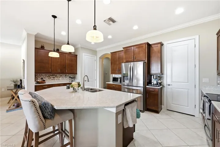 Kitchen featuring arched walkways, a breakfast bar, tasteful backsplash, an island with sink, and stainless steel fridge
