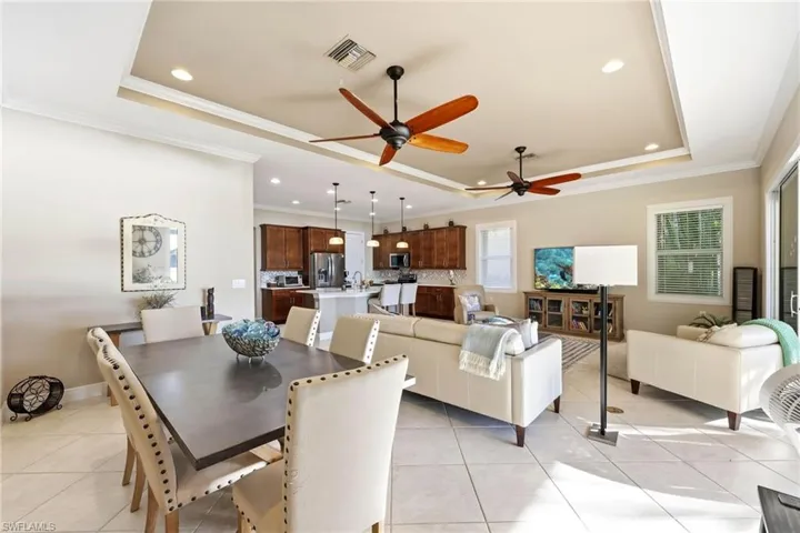 Dining area featuring a tray ceiling, light tile patterned floors, ceiling fan, crown molding, and recessed lighting
