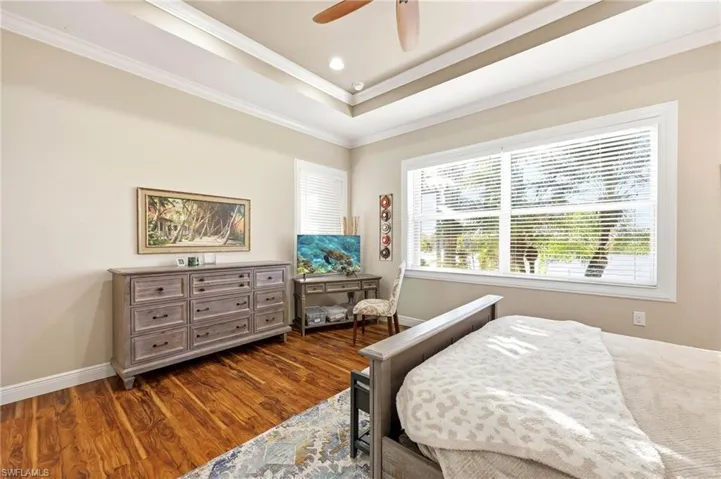 Bedroom with dark wood finished floors, ornamental molding, ceiling fan, a tray ceiling, and recessed lighting