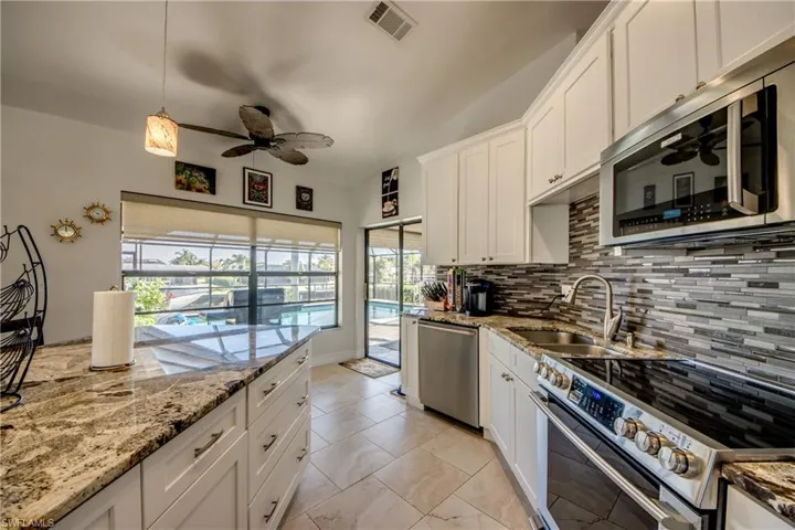 Kitchen with sink, appliances with stainless steel finishes, white cabinetry, light stone countertops, and decorative backsplash