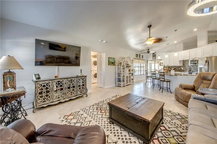 Living room featuring stacked washer and dryer, vaulted ceiling, light tile patterned flooring, and ceiling fan