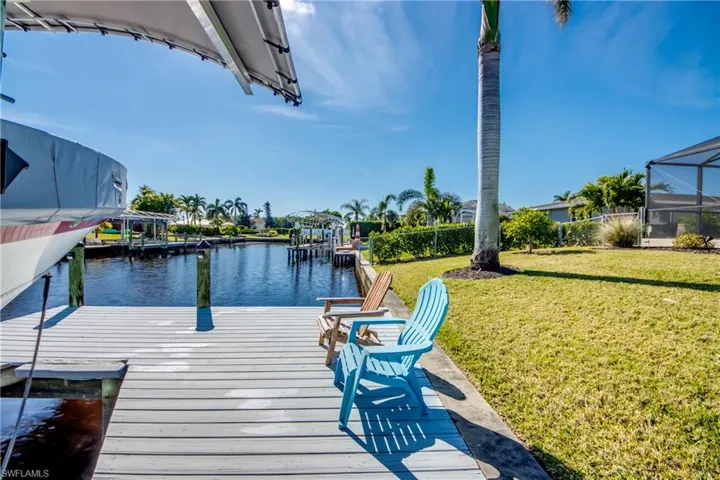 View of dock with a lanai, a lawn, and a water view