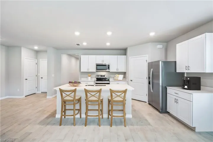 Kitchen with stainless steel appliances, light hardwood / wood-style flooring, white cabinets, a breakfast bar area, and an island with sink