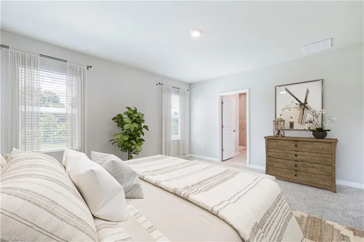 Carpeted bedroom featuring ensuite bath and multiple windows