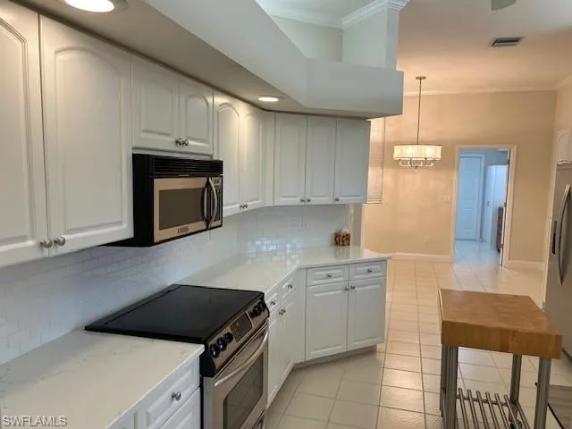 Kitchen featuring appliances with stainless steel finishes, white cabinetry, ornamental molding, light stone counters, and light tile patterned floors