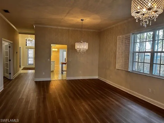 Unfurnished dining area with a chandelier, ornamental molding, dark wood-style floors, and plenty of natural light
