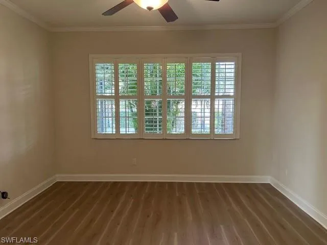 Spare room featuring healthy amount of natural light, ornamental molding, ceiling fan, and dark wood-style flooring