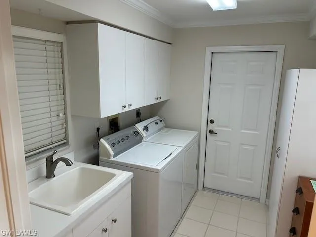Laundry area with separate washer and dryer, crown molding, light tile patterned floors, and cabinet space