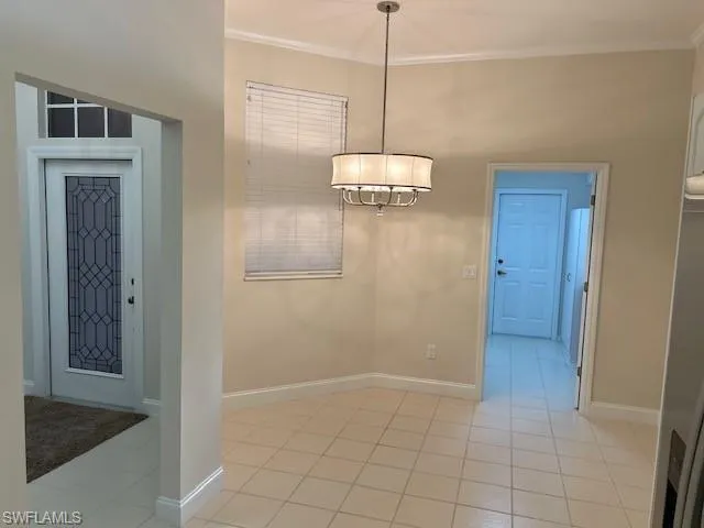 Unfurnished dining area with ornamental molding, light tile patterned floors, and a chandelier