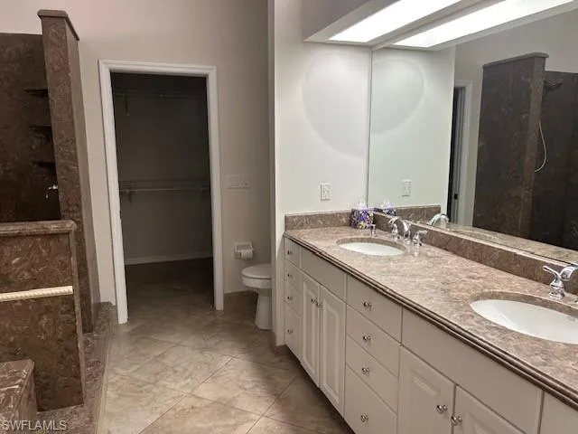 Full bath featuring tiled shower, double vanity, and a spacious closet