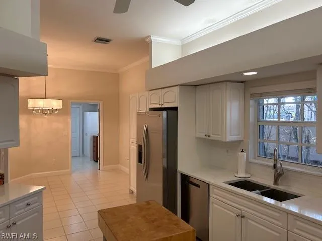 Kitchen with white cabinets, crown molding, stainless steel appliances, light stone countertops, and backsplash