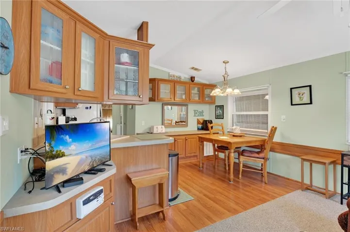 Kitchen with glass insert cabinets, light countertops, vaulted ceiling, hanging light fixtures, and light wood finished floors