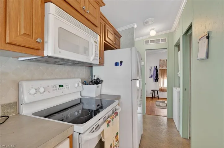 Kitchen with white appliances, crown molding, brown cabinetry, and light countertops