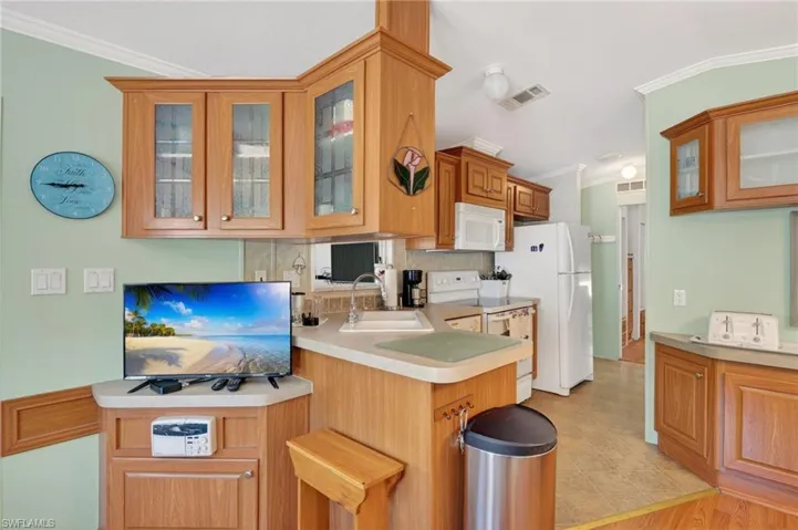 Kitchen featuring glass insert cabinets, crown molding, brown cabinetry, white appliances, and backsplash