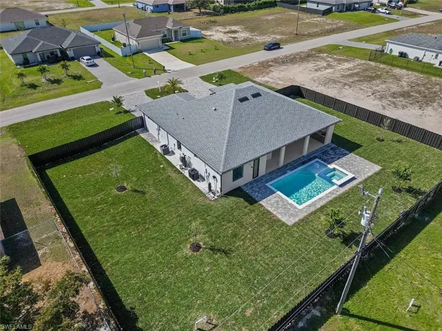 Aerial view of a residential property featuring a fenced backyard, an in-ground swimming pool with integrated spa, a paved patio, and a covered lanai
