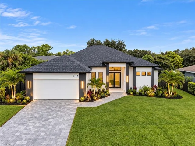 Single-story residence featuring a contrasting white and dark-toned stucco exterior, asphalt shingle hip roof, paver driveway, and a covered entryway with a glass-paneled front door
