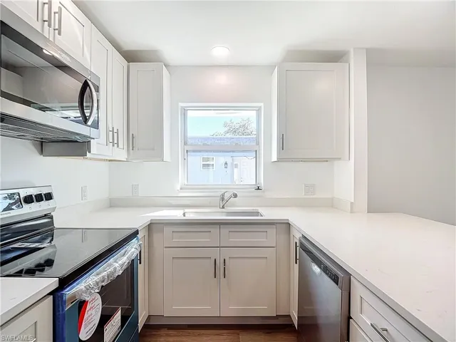 Kitchen with appliances with stainless steel finishes, light stone counters, white cabinets, dark hardwood / wood-style floors, and sink