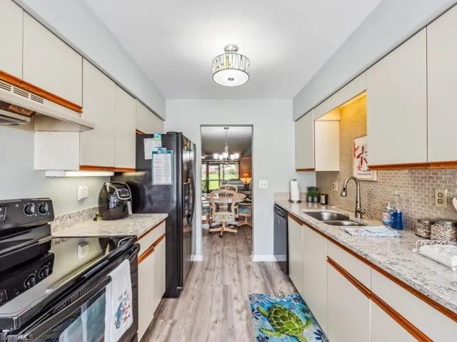 Kitchen featuring light hardwood / wood-style flooring, light stone counters, black appliances, backsplash, and sink