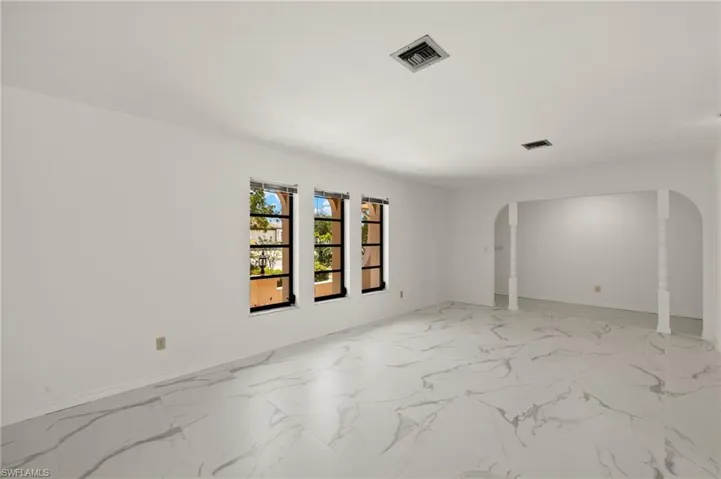 Living room featuring arched walkways, visible vents, marble-like tile finish floor, and baseboards