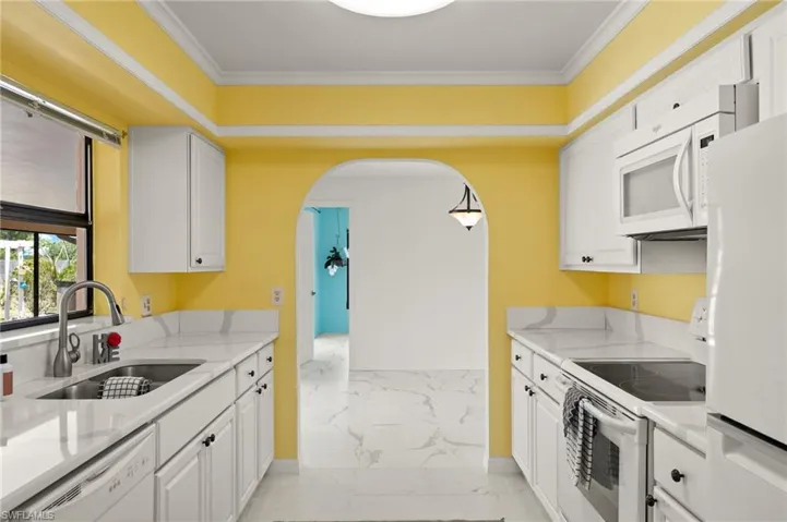 Kitchen featuring white cabinets, marble finish floor, a sink, arched walkways, and white appliances