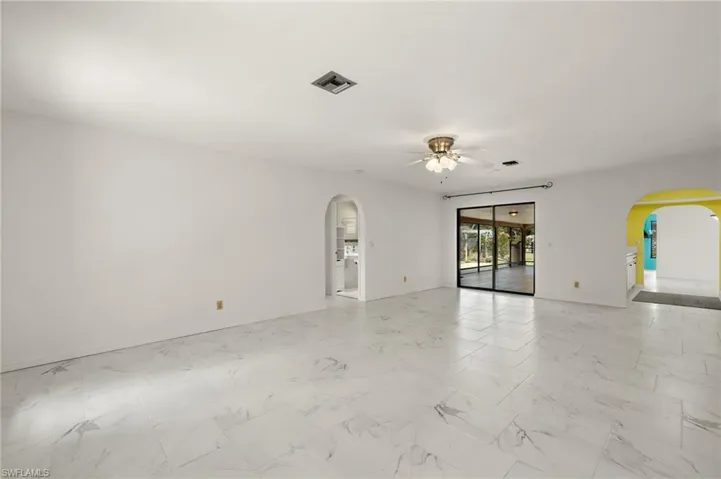 Family room with marble-like tile finish floor, visible vents, arched walkways, baseboards, and ceiling fan