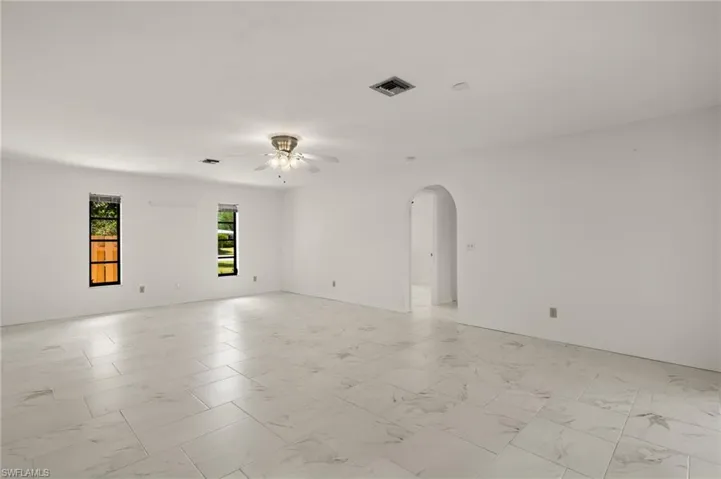 Family room featuring arched walkways, baseboards, visible vents, marble-like tile finish floor, and ceiling fan